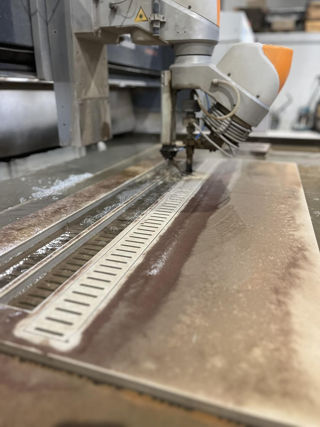 Eine Wasserstrahlschneidemaschine schneidet präzise durch Metall auf einem Maschinentisch, umgeben von einer industriellen Werkstattumgebung.