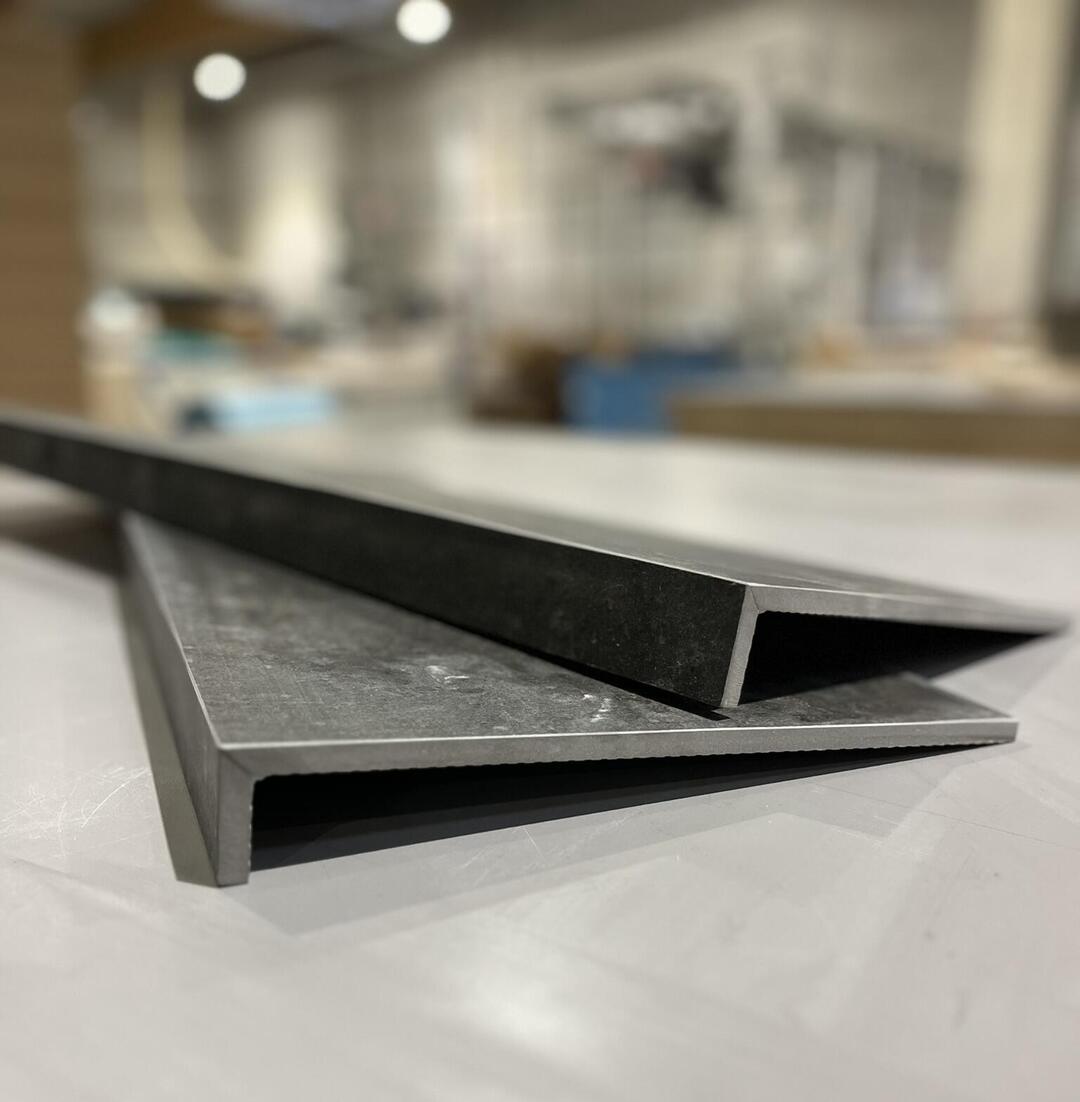 Ein Metallprofil liegt auf einem Tisch und überlappt sich leicht mit einem weiteren Profil. Die Umgebung wirkt industriell.