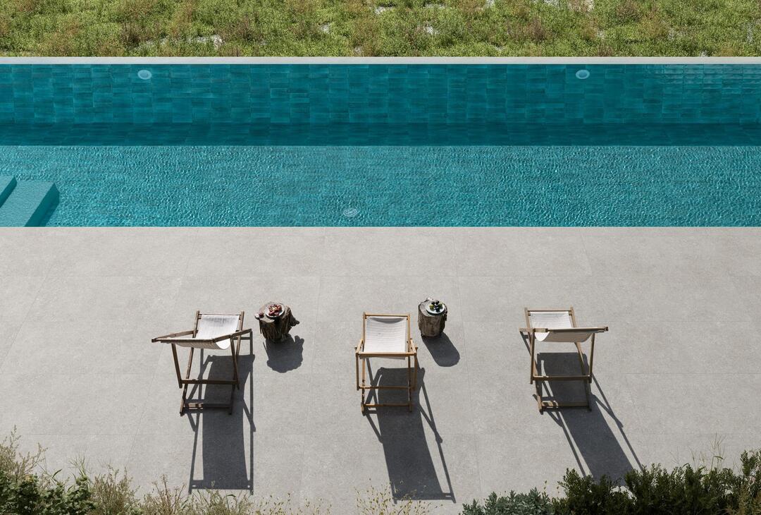 Luftaufnahme eines Pools mit türkisfarbenen Fliesen und hellgrauer Terrasse mit drei Liegestühlen