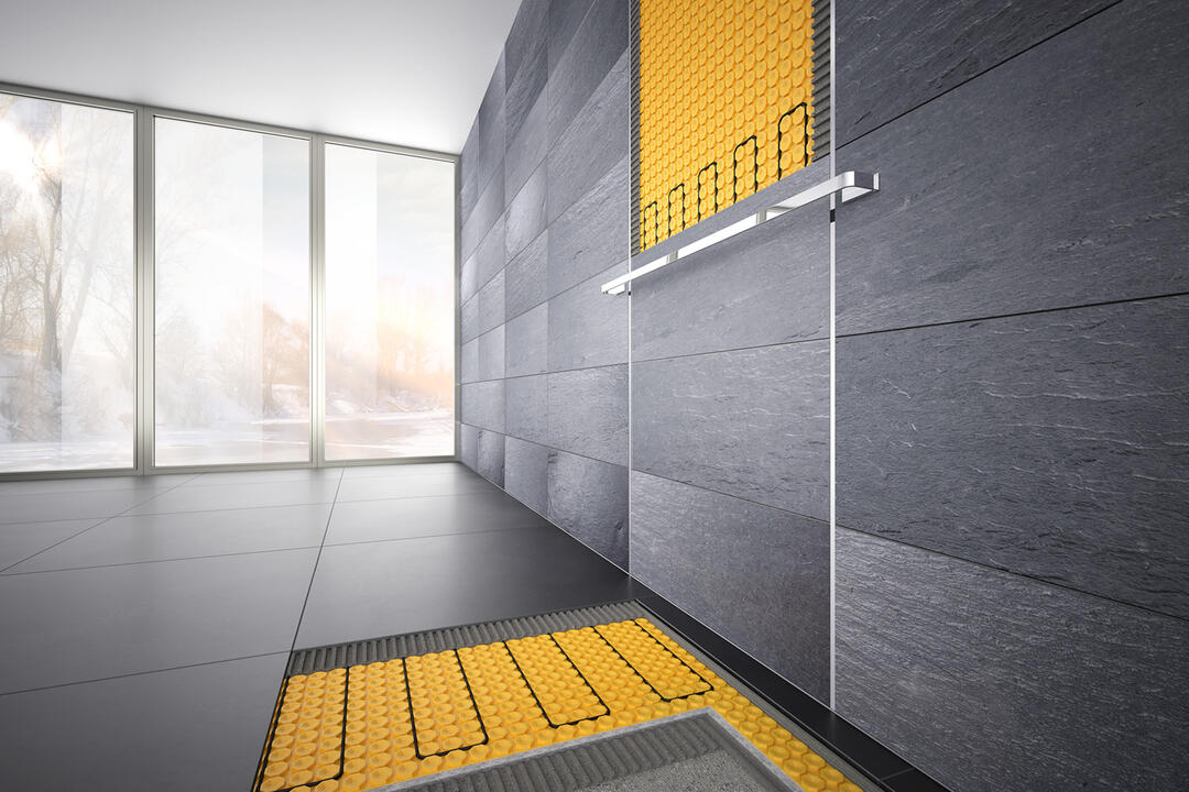 Ein großes, helles, anthrazit-farbenes Badezimmer mit großer Fensterfront, in dem einige der großformatigen Fliesen an Boden und Wand fehlen und den Blick auf den gelben Heiz-Unterbau freigeben.