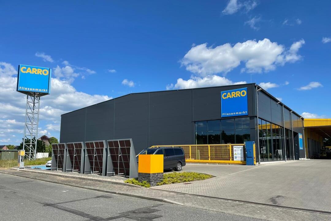 Der CARRO Fliesenmarkt in Segeberg vor blauem Himmel: Ein großes, dunkelgraues Gebäude an einer Straße, mit einem Turm, auf dem das Logo zu sehen ist.