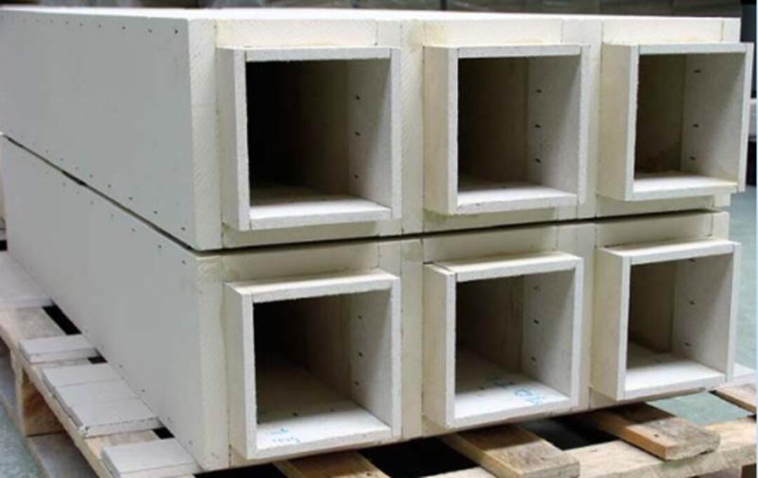 Mehrere gestapelte rechteckige Kanäle aus hellem Material liegen auf einer Holzpalette in einer industriellen Umgebung. Die Öffnungen der Kanäle sind nach vorne gerichtet.